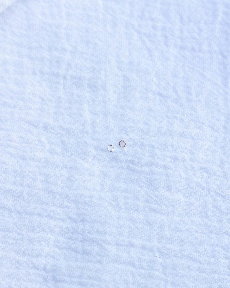 May include: Two small hoop earrings, one silver and one gold, on a white fabric background.