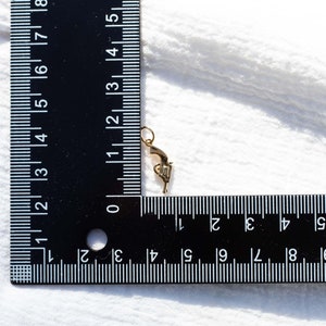 Pode incluir: Um amuleto dourado em forma de pistola, medido com uma r&eacute;gua. O amuleto mede aproximadamente 3,8 cm de comprimento.