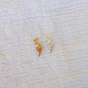 Pode incluir: Dois pingentes de prata em forma de rev&oacute;lver. Um pingente &eacute; dourado e o outro &eacute; prateado. Os pingentes est&atilde;o sobre um fundo branco.