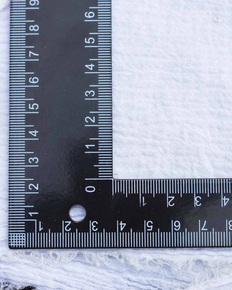 May include: A black ruler with white markings is placed on a white fabric surface. The ruler is marked in inches and centimeters. The ruler is positioned at a 90-degree angle.