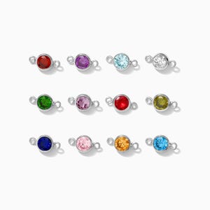 May include: Twelve silver connector charms with different colored gemstones. The charms have two loops on either side for attaching to jewelry.