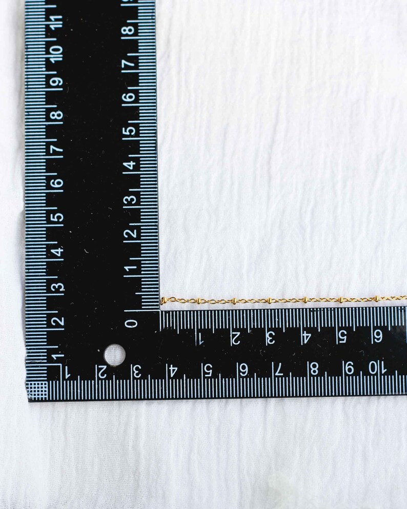 Może przedstawiać: Złoty naszyjnik w postaci łańcuszka mierzony przy użyciu czarnej linijki. Łańcuszek ma około 25 cm długości.