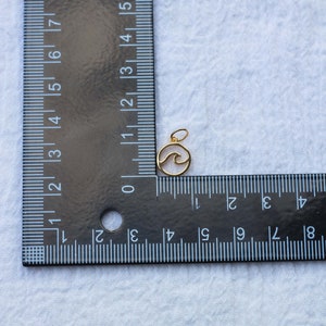 K&ouml;nnte beinhalten: Goldfarbener Anh&auml;nger mit einem Wellenmuster in einem Kreis. Der Anh&auml;nger hat einen Durchmesser von etwa 1,2 cm.