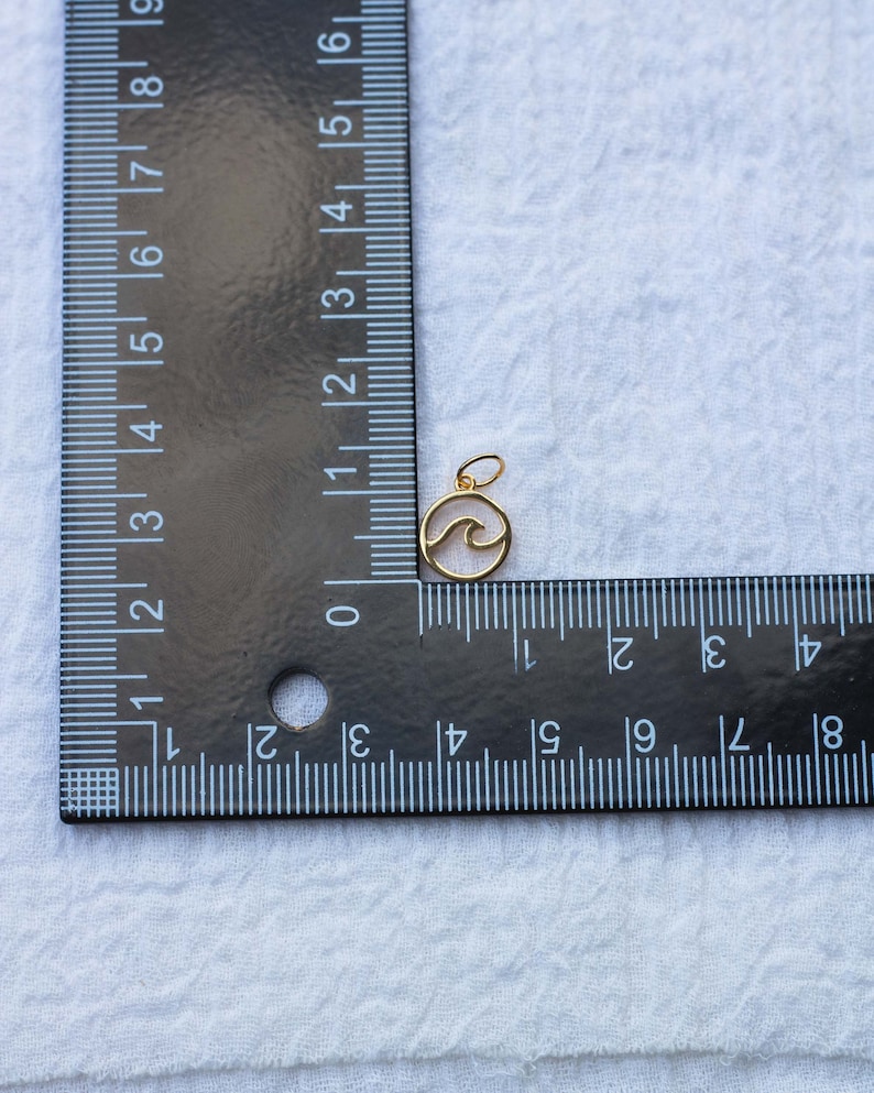 K&ouml;nnte beinhalten: Goldfarbener Anh&auml;nger mit einem Wellenmuster in einem Kreis. Der Anh&auml;nger hat einen Durchmesser von etwa 1,2 cm.