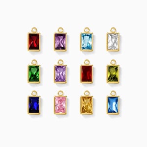 May include: A collection of rectangular gemstone charms in various colors, including red, purple, blue, and green. Each charm has a gold-colored frame and a small loop at the top for attachment. The gemstones are faceted, reflecting light.