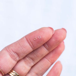 May include: Two small hoop earrings, one gold and one silver, are shown on a finger.