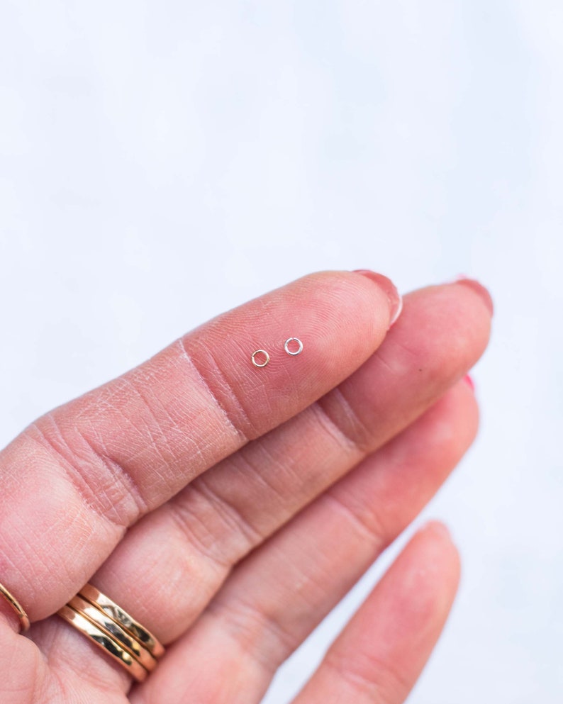 May include: Two small hoop earrings, one gold and one silver, are shown on a finger.