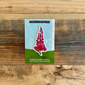 May include: Embroidered patch of a pink flower with green leaves on a white background. The patch has an iron-on backing. The text "WRENANDTHERAVEN.COM" and "EMBROIDERED PATCH WITH IRON-ON BACKING" is printed on the card.