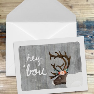 May include: A greeting card with a gray woodgrain background featuring a white reindeer with a floral crown and the text "hey you".