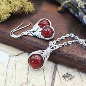 Peut inclure: Un collier et des boucles d'oreilles en argent avec des pierres de cornaline rouge enveloppées de fil d'argent. Le collier a une chaîne en argent et les boucles d'oreilles ont des crochets en argent.
