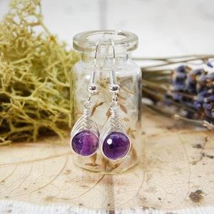 Dark purple amethyst beads wire wrapped in a herringbone design in silver wire, hang from a glass vial.