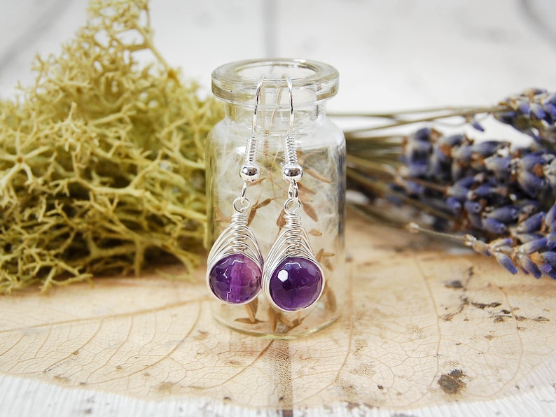 Dark purple amethyst beads wire wrapped in a herringbone design in silver wire, hang from a glass vial.