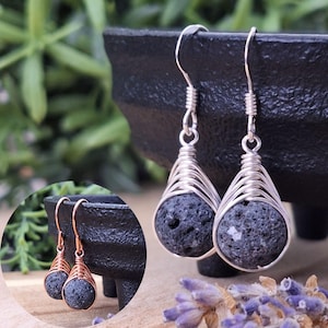 Peut inclure: Boucles d'oreilles en fil d'argent avec des perles en pierre de lave gris foncé. Les boucles d'oreilles ont une forme de goutte d'eau, la pierre de lave étant enfermée dans un design en fil tissé. Les crochets d'oreilles sont en argent.