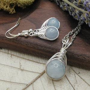 May include: A silver necklace and earrings set with light blue aquamarine stones wrapped in silver wire.
