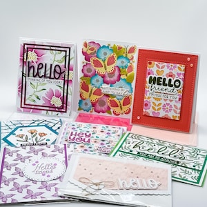 May include: A collection of handmade greeting cards featuring various floral and butterfly patterns. The cards display sentiments such as hello, thinking of you today, fluttering by just to say hi, hello friend, I'm here for you, hey you, and you are so amazing.