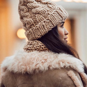 May include: A woman wearing a brown knitted hat and matching scarf, with a brown faux fur collar jacket.