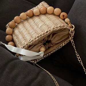 May include: A small straw bag with a wooden bead handle and a gold chain strap. The bag has a drawstring closure and a brown lining.