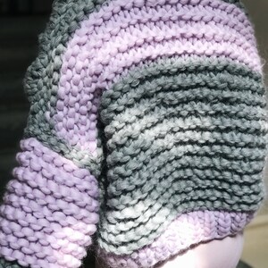 May include: A chunky knit sweater with a striped pattern in shades of grey and lavender.