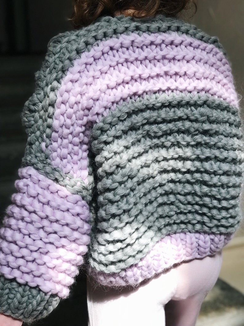 May include: A chunky knit sweater with a striped pattern in shades of grey and lavender.