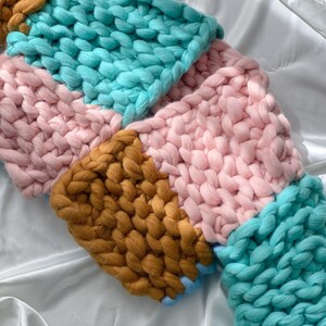 Pode incluir: Uma manta de malha grossa com um design de patchwork em tons de rosa, turquesa e marrom.