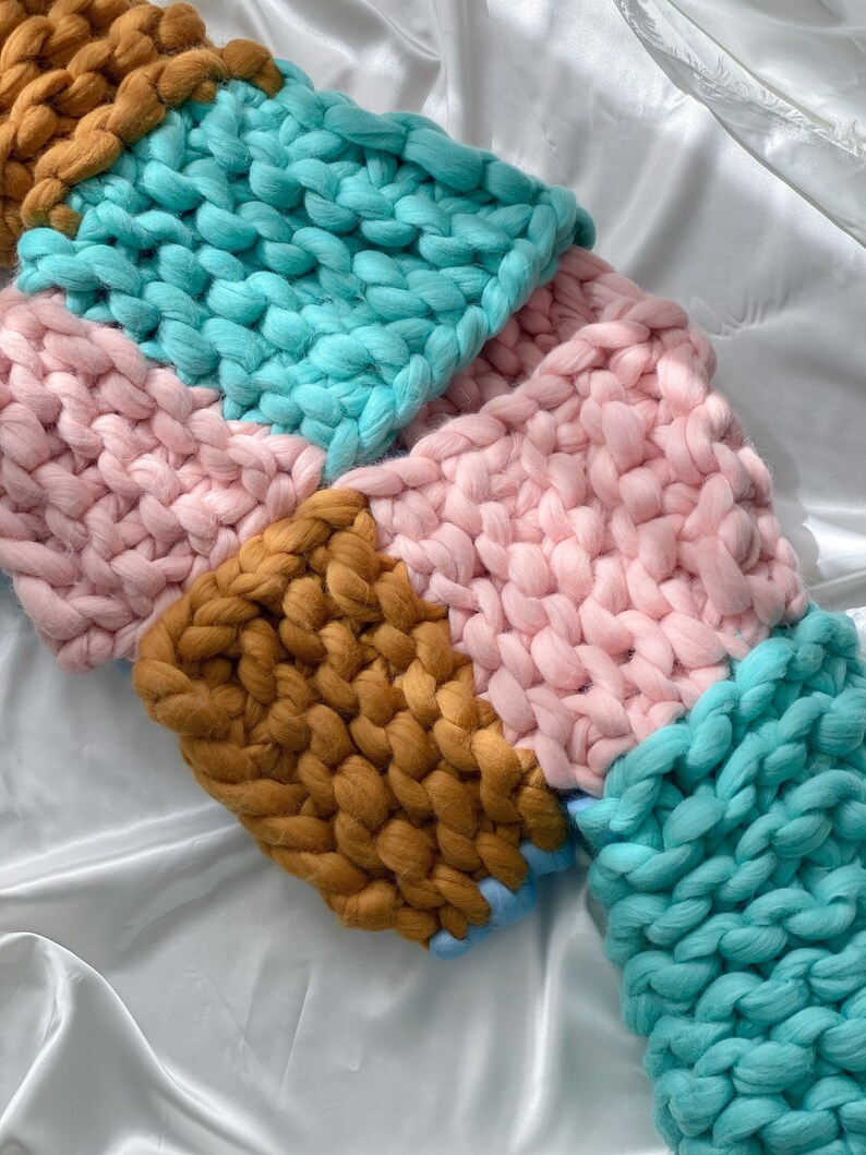 Pode incluir: Uma manta de malha grossa com um design de patchwork em tons de rosa, turquesa e marrom.