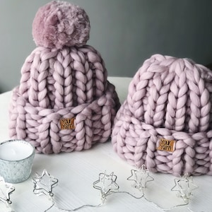 May include: Two pink knitted hats with pom poms. The hats are made with chunky yarn and have a brown leather tag that says "Your Yarn".