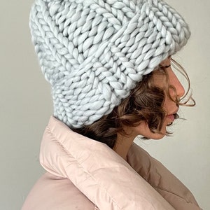 May include: A light grey chunky knit beanie hat. The hat is made with a thick yarn and has a slouchy fit.