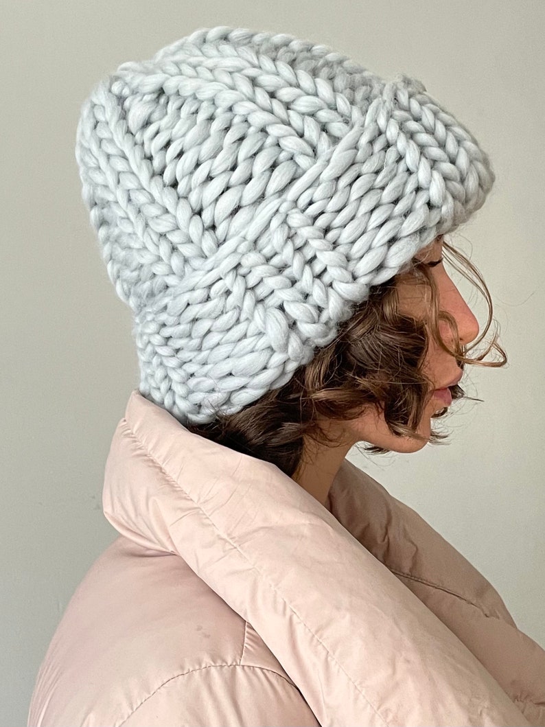 May include: A light grey chunky knit beanie hat. The hat is made with a thick yarn and has a slouchy fit.