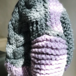 May include: A chunky knit sweater with a colour block design. The sweater is made of a soft, fluffy yarn and has a relaxed fit. The sweater is grey and purple.