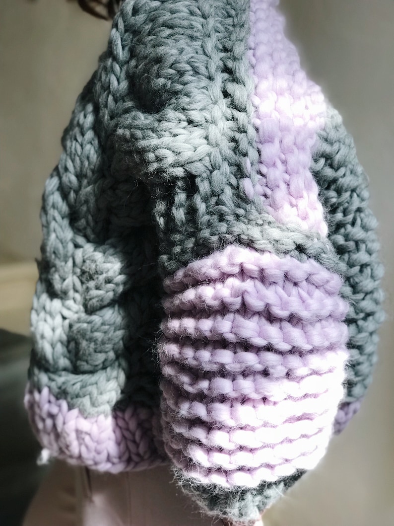 May include: A chunky knit sweater with a colour block design. The sweater is made of a soft, fluffy yarn and has a relaxed fit. The sweater is grey and purple.