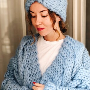 May include: A light blue knitted headband and a matching chunky knit cardigan. The cardigan has a loose fit and a v-neck.