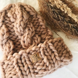 May include: A chunky knit beanie in a light brown color with a leather tag that says "Your Yarn".