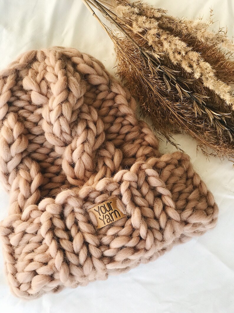 May include: A chunky knit beanie in a light brown color with a leather tag that says "Your Yarn".