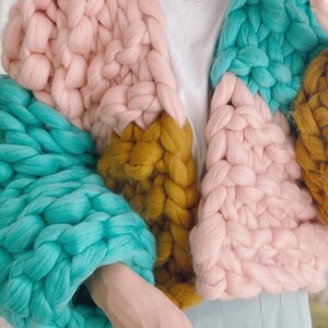 Pode incluir: Um casaco de malha grossa com um design de blocos de cores em rosa, azul-turquesa e amarelo mostarda.