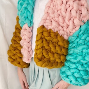 Pode incluir: Um casaco de malha grossa com um design de blocos de cores em turquesa, rosa e amarelo mostarda.
