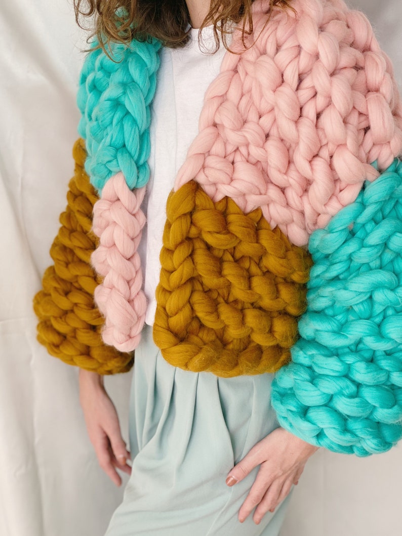 Pode incluir: Um casaco de malha grossa com um design de blocos de cores em turquesa, rosa e amarelo mostarda.