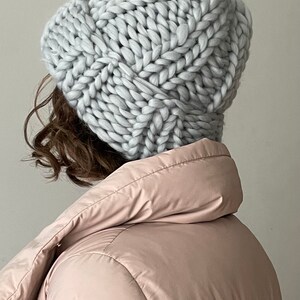 May include: A light grey chunky knit beanie hat with a cable knit pattern.