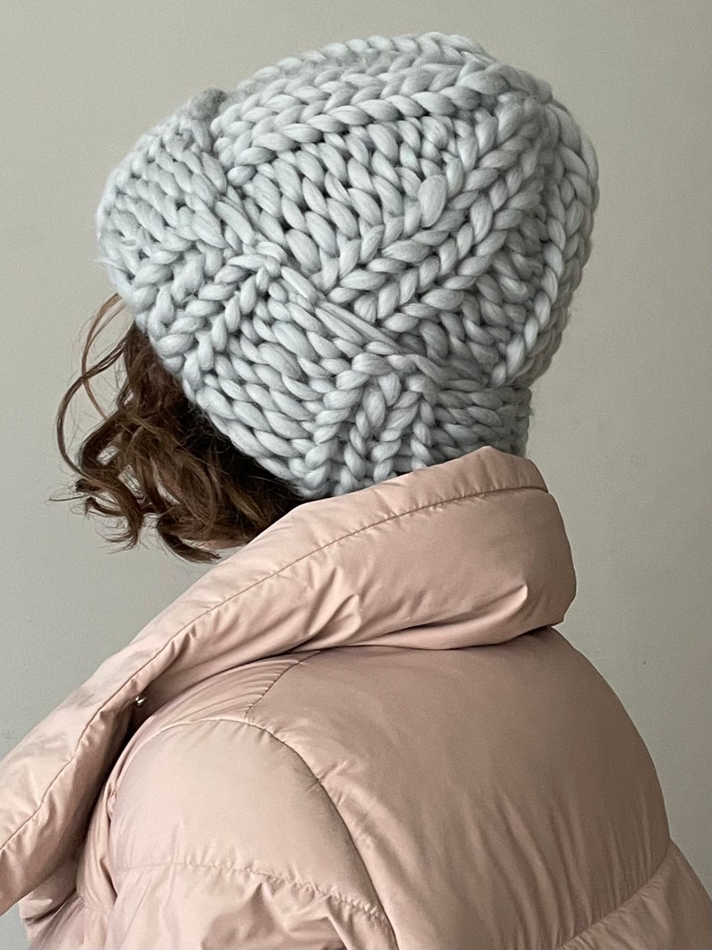 May include: A light grey chunky knit beanie hat with a cable knit pattern.