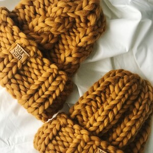 May include: Two mustard yellow knitted hats with a cable knit pattern. Each hat has a brown leather tag with the text "Your Yarn" on it.