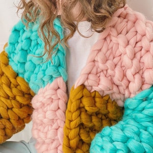 Pode incluir: Um casaco de malha grossa com um design de blocos de cores em turquesa, rosa e amarelo mostarda.