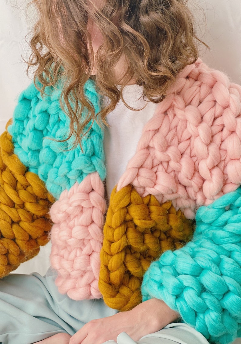 Pode incluir: Um casaco de malha grossa com um design de blocos de cores em turquesa, rosa e amarelo mostarda.