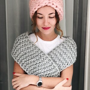 May include: A woman wearing a pink knitted headband and a gray knitted scarf. She is wearing a white t-shirt and a silver watch.
