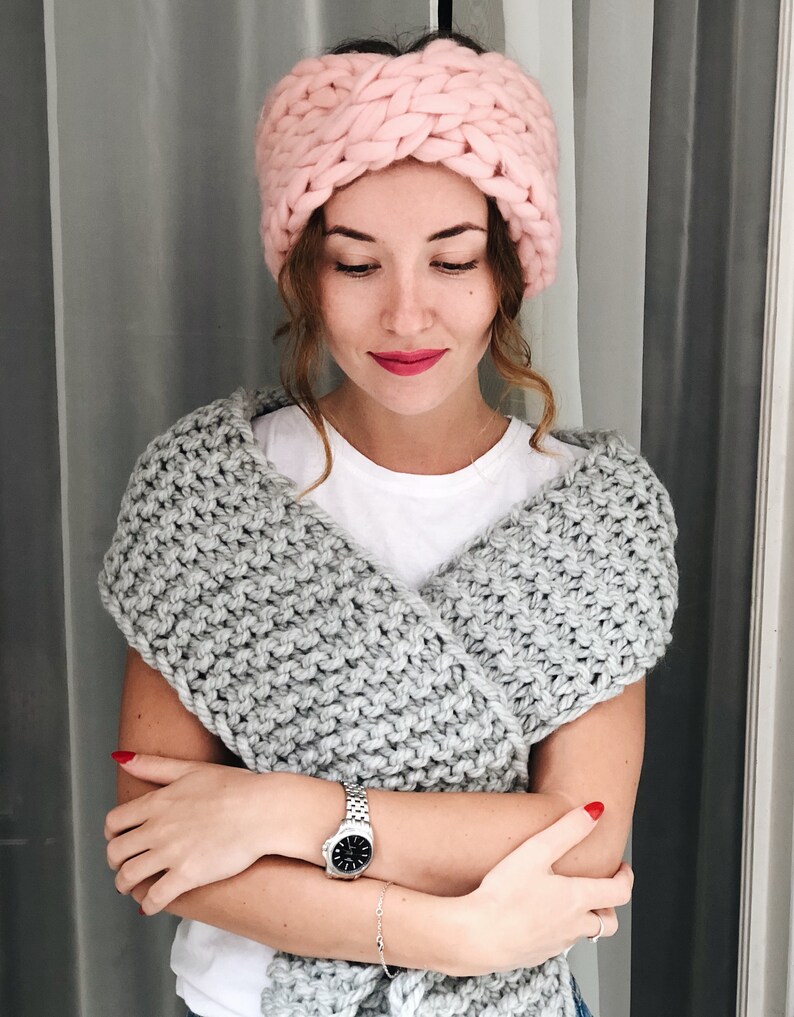 May include: A woman wearing a pink knitted headband and a gray knitted scarf. She is wearing a white t-shirt and a silver watch.