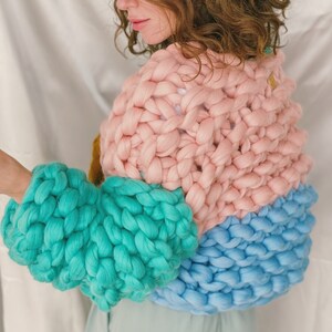 Pode incluir: Um su&eacute;ter de tric&ocirc; grosso com um design de blocos de cores rosa, turquesa e azul. O su&eacute;ter tem um caimento solto e &eacute; feito de um fio macio e aconchegante.
