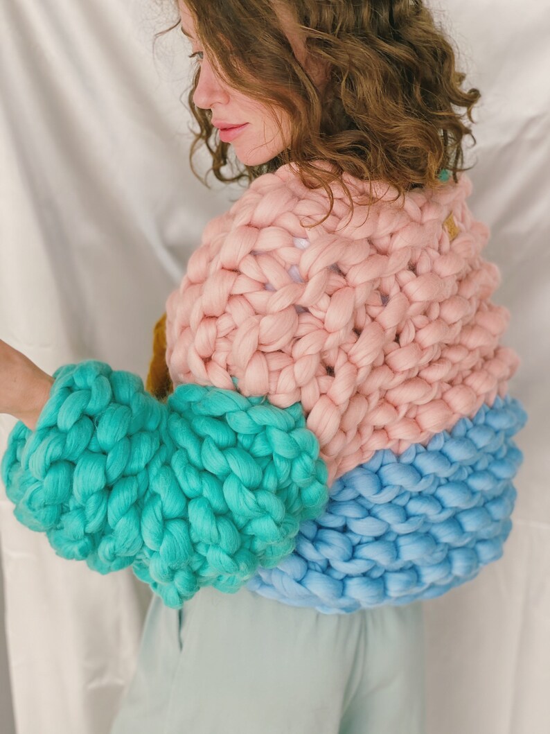 Pode incluir: Um su&eacute;ter de tric&ocirc; grosso com um design de blocos de cores rosa, turquesa e azul. O su&eacute;ter tem um caimento solto e &eacute; feito de um fio macio e aconchegante.