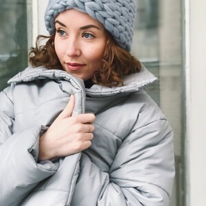 May include: A woman wearing a light blue knitted headband and a light blue puffer jacket.