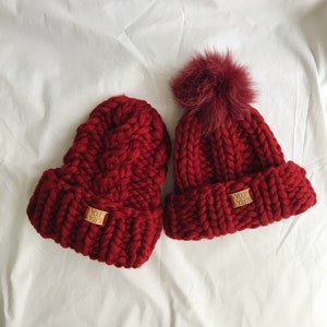 May include: Two red knitted beanies with pom poms. One beanie has a "Your Yarn" label.