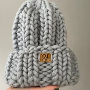May include: A grey knitted beanie with a brown leather tag that says "Your Yarn".