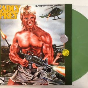 May include: A VHS tape cover for the action-adventure movie "Deadly Prey". The cover features a muscular man holding a gun, with a helicopter flying overhead. The text "Deadly Prey" is in large, bold letters at the top of the cover, and the text "VHS" is in the bottom left corner.