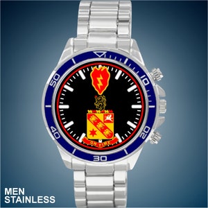 May include: A silver stainless steel watch with a black face and blue bezel. The face features a military unit crest with a red heart, lightning bolt, and a yellow and red shield. The watch face also has the words "On Time" printed on it.